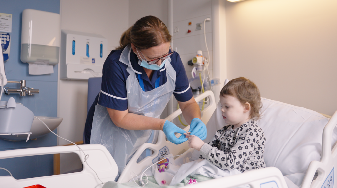 Nurse checking observations with young patient in hospital bed